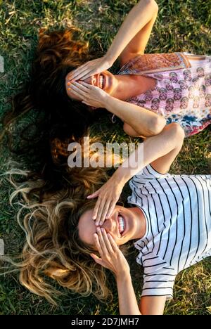 Giovani donne allegre che coprono gli occhi con le mani mentre si sdraia campo Foto Stock