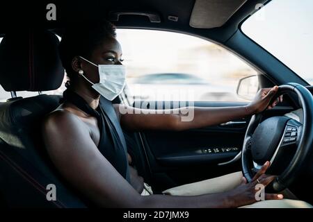 Giovane donna che indossa la maschera facciale concentrandosi sulla guida dell'auto Foto Stock