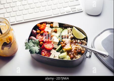 Pranzo al sacco con insalata vegana fresca sdraiata sulla scrivania parte anteriore della tastiera del computer Foto Stock