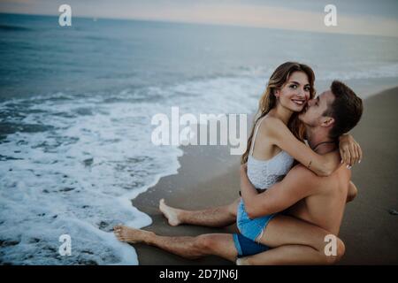Uomo che baciava la donna seduta in grembo sulla spiaggia Foto Stock