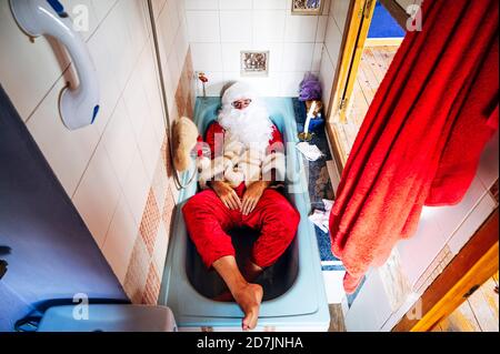 Uomo che indossa il costume di Babbo Natale sdraiato nella vasca da bagno a casa Foto Stock