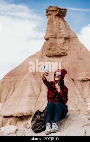 Spagna, Navarra, Ritratto di turista femminile prendendo selfie di fronte alla formazione di pietra arenaria in Bardenas Reales Foto Stock