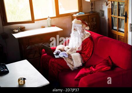 Uomo che indossa il costume di Babbo Natale utilizzando il computer portatile mentre si siede divano a casa Foto Stock