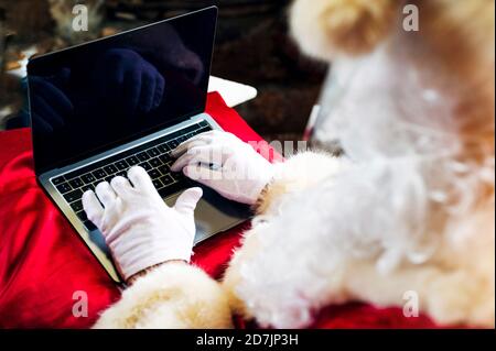 Uomo che indossa il costume di Babbo Natale utilizzando il computer portatile mentre si siede a. casa Foto Stock