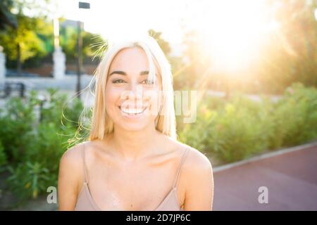 Primo piano di una giovane donna sorridente con capelli biondi nel parco durante il tramonto Foto Stock