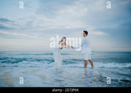 Una coppia giocosa che tiene le mani mentre si è in piedi in acqua sulla spiaggia Foto Stock