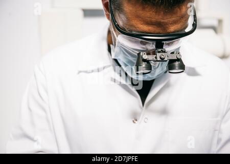 Dentista maschile nelle loupes chirurgiche e maschera che lavora in clinica Foto Stock