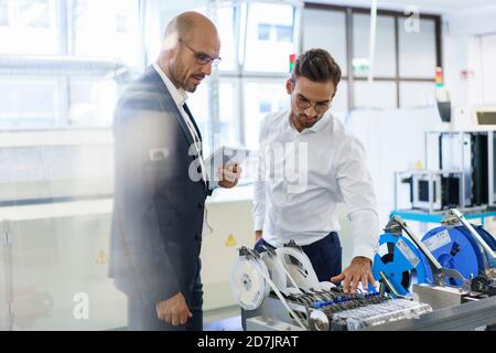 Tecnici maschi sicuri che discutono sui macchinari contro i macchinari in fabbrica Foto Stock