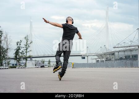 Giovane uomo con le braccia distese ascoltando musica mentre si pattina in linea su strada Foto Stock