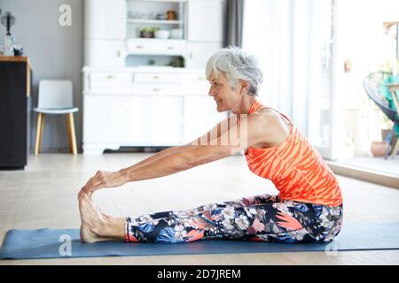 Adatta donna anziana allungando gamba e schiena mentre si esercita a. casa Foto Stock