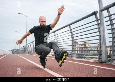 Giovane uomo inline pattinare mentre accovacciato sul ponte contro il cielo Foto Stock