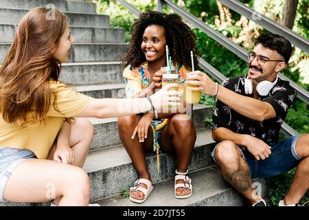 Gli amici fanno un brindisi celebrativo mentre si siedono sui gradini nel parco Foto Stock