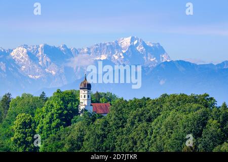 Germania, Baviera, Holzhausen, San Giovanni Battista chiesa circondata da verde foresta in estate con Zugspitze in background lontano Foto Stock