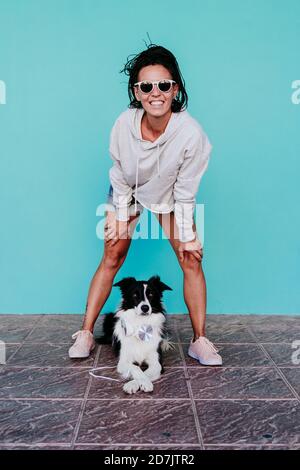 Donna felice che si piega sopra il cane di bordo Collie contro la parete turchese Foto Stock