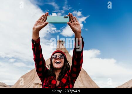 Spagna, Navarra, Ritratto di turista femminile prendendo selfie di fronte alla formazione di pietra arenaria in Bardenas Reales Foto Stock