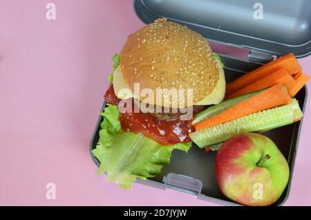 Hamburger fatti in casa con lattuga in scatola sul tavolo. Con succo d'arancia giallo brillante. Con noci alla banana. Carote e cetrioli di verdure a fette Foto Stock