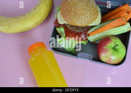 Hamburger fatti in casa con lattuga in scatola sul tavolo. Con succo d'arancia giallo brillante. Con noci alla banana. Carote e cetrioli di verdure a fette Foto Stock