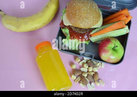 Hamburger fatti in casa con lattuga in scatola sul tavolo. Con succo d'arancia giallo brillante. Con noci alla banana. Carote e cetrioli di verdure a fette Foto Stock