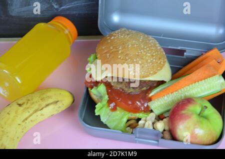 Hamburger fatti in casa con lattuga in scatola sul tavolo. Con succo d'arancia giallo brillante. Con noci alla banana. Carote e cetrioli di verdure a fette Foto Stock