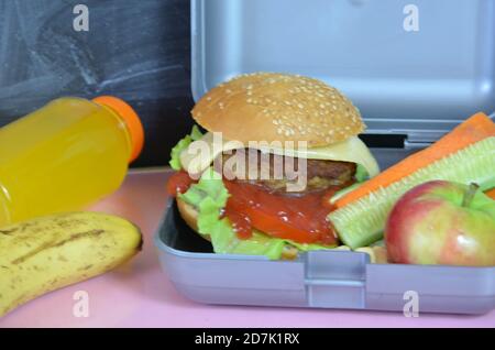 Hamburger fatti in casa con lattuga in scatola sul tavolo. Con succo d'arancia giallo brillante. Con noci alla banana. Carote e cetrioli di verdure a fette Foto Stock