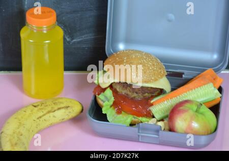 Hamburger fatti in casa con lattuga in scatola sul tavolo. Con succo d'arancia giallo brillante. Con noci alla banana. Carote e cetrioli di verdure a fette Foto Stock