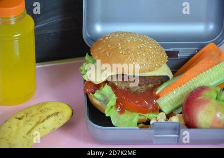 Hamburger fatti in casa con lattuga in scatola sul tavolo. Con succo d'arancia giallo brillante. Con noci alla banana. Carote e cetrioli di verdure a fette Foto Stock