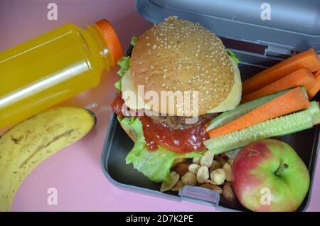 Hamburger fatti in casa con lattuga in scatola sul tavolo. Con succo d'arancia giallo brillante. Con noci alla banana. Carote e cetrioli di verdure a fette Foto Stock