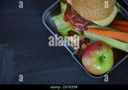 Hamburger fatti in casa con lattuga in scatola. Con succo d'arancia. Noci di banana. Carote di verdure e cetrioli. Sulla lavagna nera della scuola. Snack Foto Stock