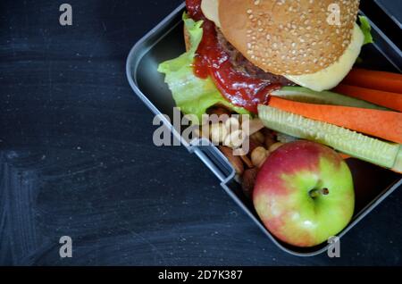 Hamburger fatti in casa con lattuga in scatola. Con succo d'arancia. Noci di banana. Carote di verdure e cetrioli. Sulla lavagna nera della scuola. Snack Foto Stock
