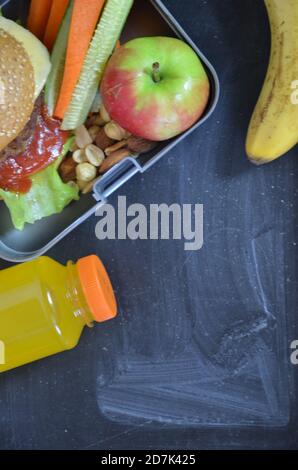 Hamburger fatti in casa con lattuga in scatola. Con succo d'arancia. Noci di banana. Carote di verdure e cetrioli. Sulla lavagna nera della scuola. Snack Foto Stock