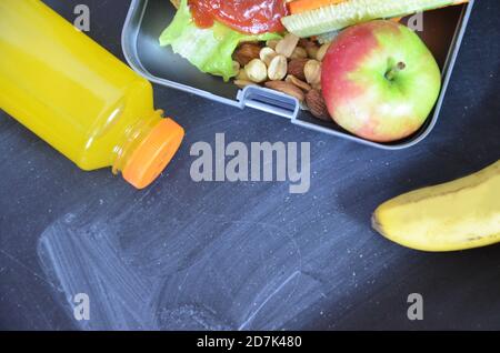Hamburger fatti in casa con lattuga in scatola. Con succo d'arancia. Noci di banana. Carote di verdure e cetrioli. Sulla lavagna nera della scuola. Snack Foto Stock
