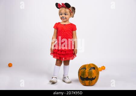 Ragazza in abito rosso si trova accanto a una grande zucca dipinta. Giorno d'autunno. Divertimento di Halloween. Foto su sfondo bianco Foto Stock