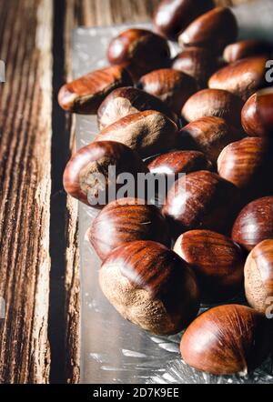 primo piano di diverse castagne in un piatto di vetro, su un tavolo di legno. Porta Foto Stock