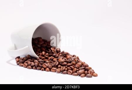 Chicchi di caffè isolati (fuoco selettivo sui chicchi di caffè) con tazza in ceramica, fondo bianco. Foto Stock