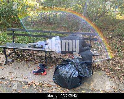 L'uomo senza dimora dorme su una panchina nel Prospect Park con un arcobaleno sopra di lui. Brooklyn, New York Foto Stock