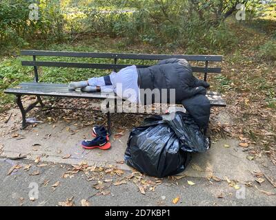 L'uomo senza dimora dorme su una panchina nel Prospect Park durante l'autunno a Brooklyn, New York. Foto Stock