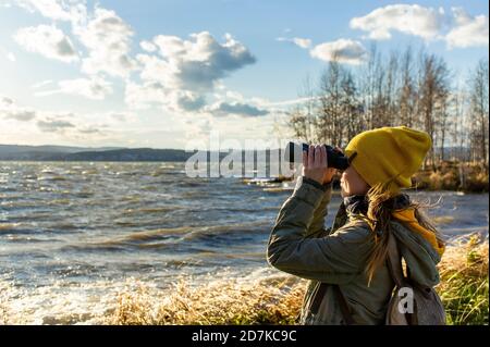 Giovane donna che guarda attraverso il binocolo agli uccelli sul lago. Birdwatching, zoologia, ecologia. Ricerca, osservazione di animali. Ornitologia Foto Stock