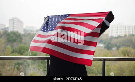 Afroamericano che alza la bandiera nazionale degli Stati Uniti sul balcone. Foto di alta qualità Foto Stock