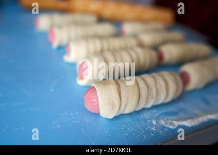 Sbozzati per torte fritte. Le salsicce sono avvolte in sottili strisce di impasto di lievito. L'impasto si sta alzando. Spazio di copia, messa a fuoco selettiva Foto Stock