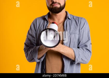 un uomo bearded in una camicia casual con un altoparlante nelle sue mani grida in un megafono su un giallo sfondo Foto Stock