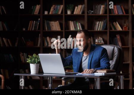 Entusiasta giovane imprenditore vincitore guarda portatile festeggia Bid vincere il successo online vincere una nuova opportunità di sedersi in ufficio Foto Stock