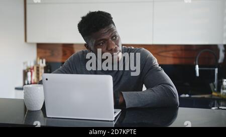 giovane uomo nero afroamericano che lavora su un computer portatile nel suo appartamento che si allunga e guarda attraverso la finestra. Foto di alta qualità Foto Stock