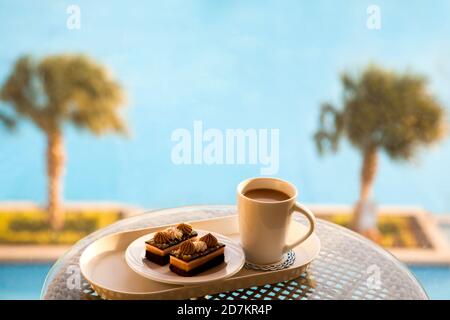Caffè pomeridiano con americano caldo con latte, brownie al cioccolato in piscina sullo sfondo del resort dell'hotel. Foto Stock