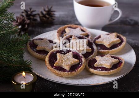 Biscotti natalizi con confettura di mirtilli, cosparsi di zucchero in polvere su un tavolo di legno con decorazioni natalizie tradizionali Foto Stock