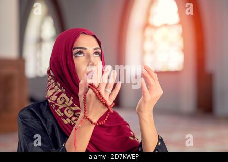 Giovane musulmana che legge il Corano nella moschea e alla luce del sole caduta dal finestrino Foto Stock