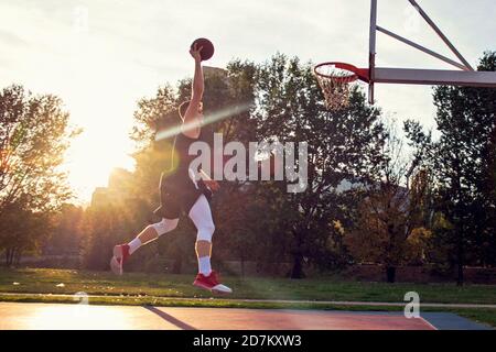 Giovane uomo di salto e facendo un fantastico Slam Dunk giocando streetball, basket. Urban autentica. Foto Stock