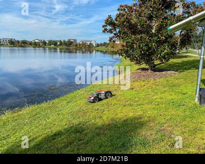 Orlando, FL./USA - 10/16/20: Falciatrice autonoma Husqvarna vicino ad un lago nel quartiere di Laureate Park a Orlando, Florida Foto Stock