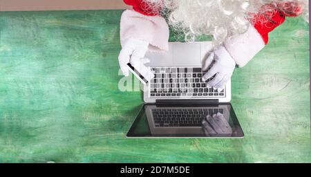 Vista dall'alto di Babbo Natale lavorando con le mani su un computer portatile che effettua acquisti con una carta di credito dorata, è possibile vedere un dettaglio della sua barba. Spazio di testo Foto Stock