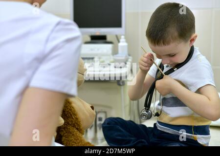 Il medico e un ragazzo, con la testa piegata in tasca, inseriscono una spatola medica. In clinica per consultazione. Foto Stock