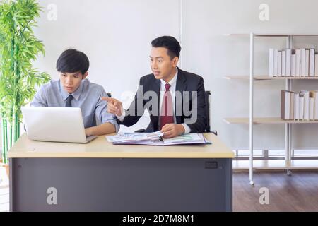 Un supervisore maschile asiatico insegna il nuovo arrivato all'ufficio sulla sua scrivania. Foto Stock